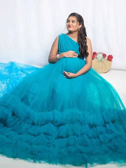 A classic solo maternity portrait. The client looks serene and beautiful in a vibrant blue gown with a long trail, creating a striking contrast against the simple white backdrop.