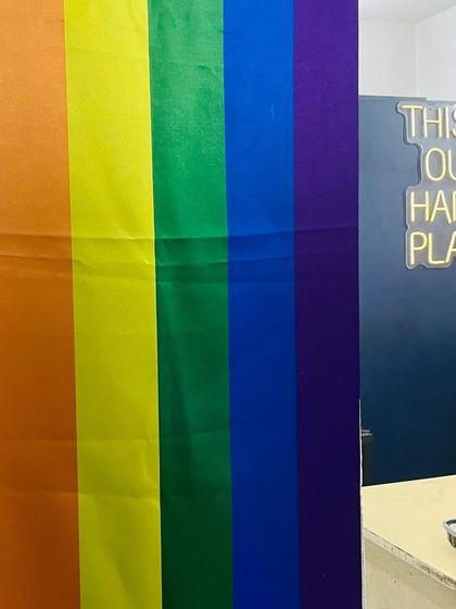 Our "This Is Our Happy Place" neon sign next to a rainbow flag. This is the motto of our kitchen and our lives.