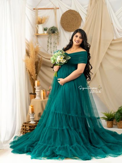 Holding a bouquet, the mother-to-be glows in this emerald green gown, surrounded by soft, warm light.