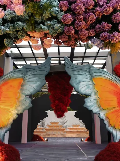 A dramatic entrance featuring giant butterfly wings and a cascade of red flowers. This is an example of how I use bold, artistic elements to create unforgettable, high-impact decor.