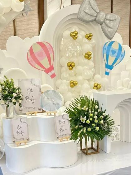 A wide shot of the elegant white baby shower setup, showing the welcome area with multiple signs and displays. This creates a cohesive and inviting entrance for guests.