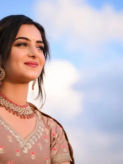 A beautiful portrait of the model against a blue sky, the lighting highlighting her features and jewelry.