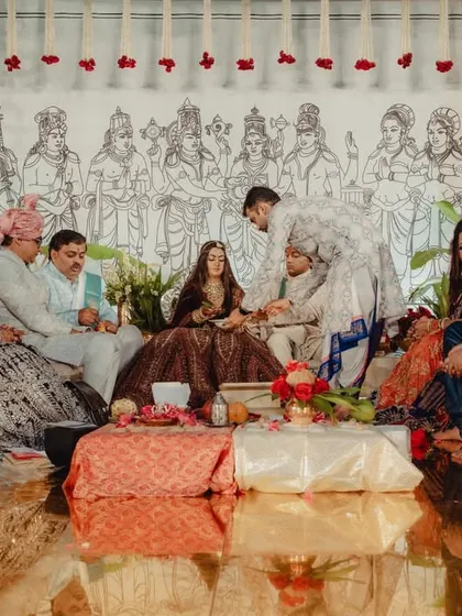 The couple and their families engaged in the wedding rituals inside the ornate mandap. The image captures the intimate nature of the ceremony against the grandeur of the surrounding decor.