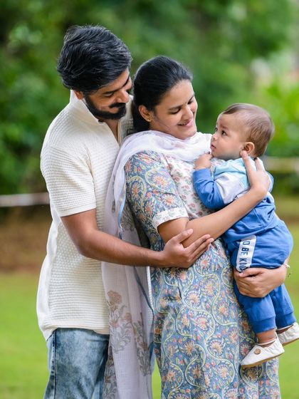 A beautiful, classic family portrait taken outdoors. The parents look lovingly at their child, creating a timeless image of family connection and love.