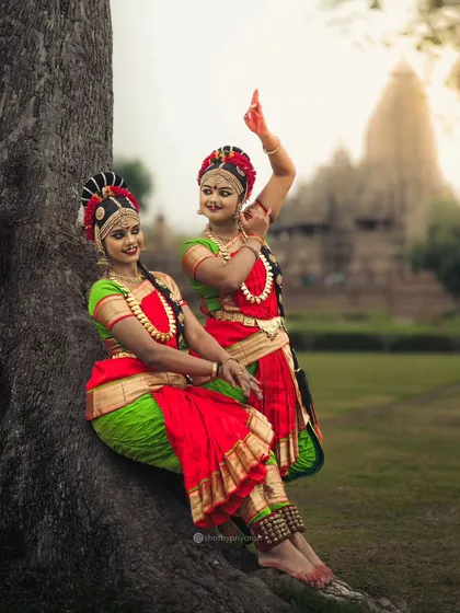 Kuchipudi dancers posing gracefully by a tree at the Khajuraho temple complex, a perfect blend of nature and culture.