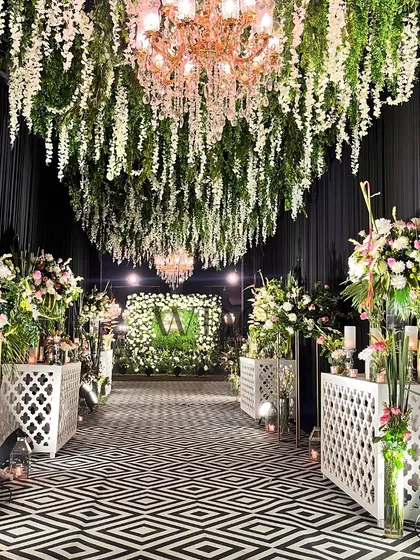 We love to make a bold statement. This striking entrance features a ceiling of cascading wisteria, a modern black and white geometric floor, and lush floral arrangements, creating a high contrast, luxurious welcome for a grand reception.