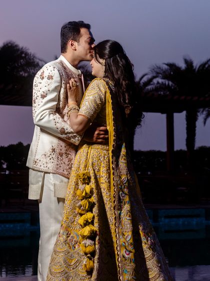 A romantic moment against the twilight sky. The groom's ivory and pink Jatin Malik jacket picks up the delicate embroidery in the bride's stunning yellow Nidhi Tholia lehenga.