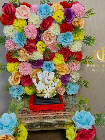 A dense and colorful wall of flowers creates a stunning backdrop for this Ganpati idol. This design is perfect for making a bold and festive statement in your home during Ganesh Chaturthi.