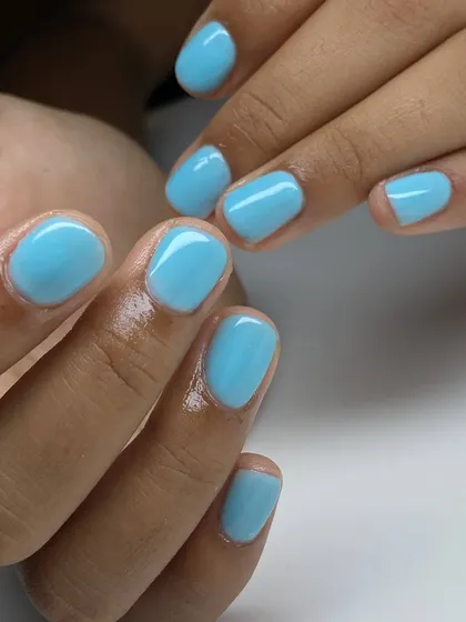 A bright, pastel blue manicure on short, rounded nails. This fun and fresh color is perfect for a playful and modern look.