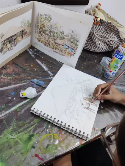 A young student works on a detailed landscape drawing with color pencils, learning to recreate a complex scene from a reference photo.