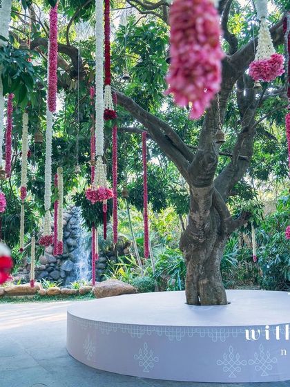 A tree at the wedding venue decorated with hanging floral garlands, creating a beautiful and festive atmosphere.