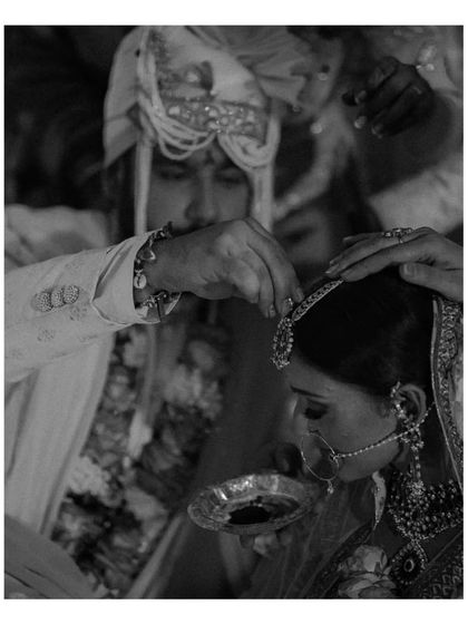 A black and white shot of the groom applying sindoor to the bride's forehead, a significant and emotional moment in a Hindu wedding ceremony.