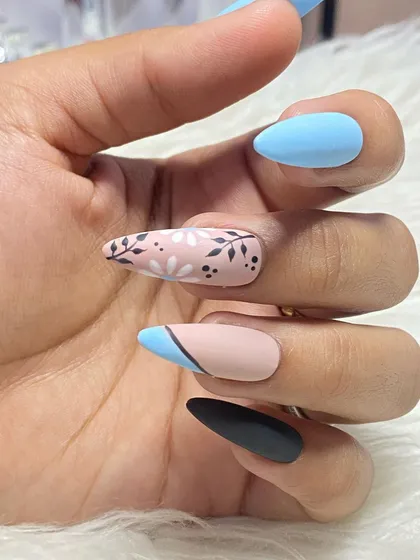 This custom press-on set features a mix of matte colors and detailed floral art. It includes solid sky blue, black, and nude nails with hand-painted daisy patterns.