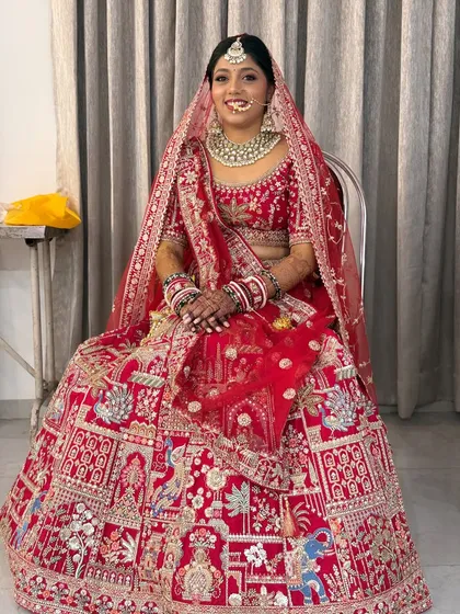 The bride seated, giving a full view of her intricately embroidered lehenga. The makeup and hair are styled to perfection.