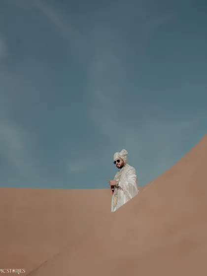 A minimalist yet powerful portrait of the groom, Jigar, against the sand dunes. The clean lines and the contrast between the blue sky and the warm sand create a striking, artistic image.