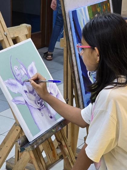 Concentration and creativity in action. A young student works diligently on her imaginative ballpoint pen drawing of animals on canvas.