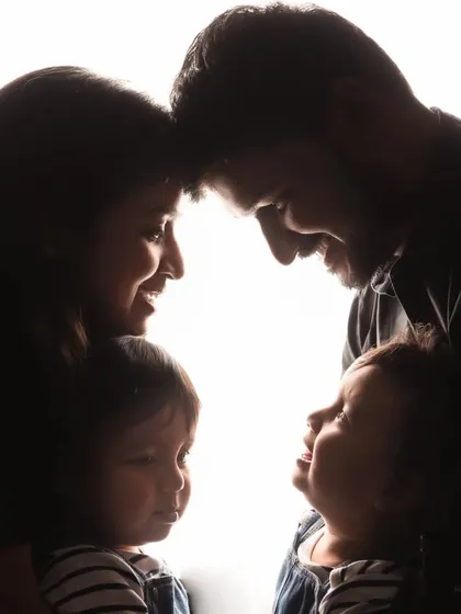 A creative silhouette portrait of a family with their twin toddlers. This artistic shot beautifully captures the outline of their connection, with the parents and children gazing at each other.