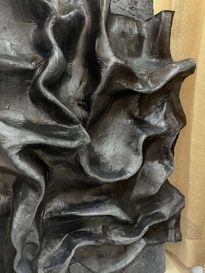 A side view of the dramatic black folded artwork, emphasizing its incredible depth and sculptural quality. It extends from the wall, creating fascinating shadows that change throughout the day.