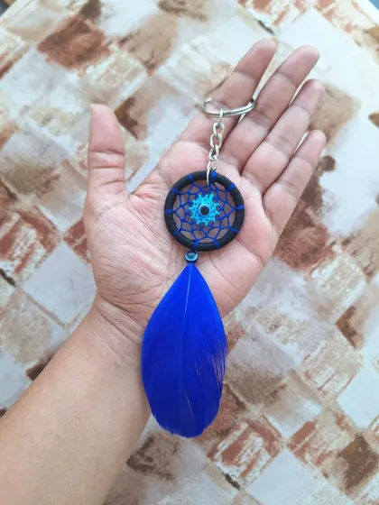 A striking dreamcatcher bag charm with a bold blue feather and a black-wrapped hoop for a dramatic look.