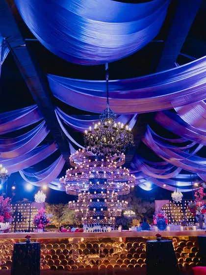 A massive, multi-tiered chandelier hangs over the bar, complemented by a ceiling of draped fabric, creating a spectacular focal point for the reception.