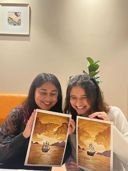 Two friends delighted with their finished coffee paintings of a ship at sea. It's a perfect activity for a creative afternoon.