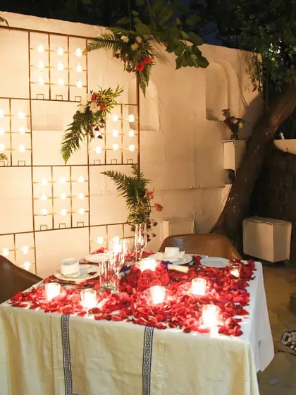 The combination of a candlelit wall, floral arrangements, and a table covered in rose petals makes for an incredibly romantic and photogenic setting.