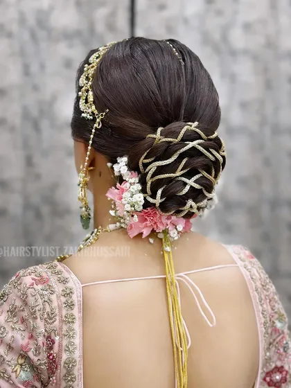 For this bridal bun, I wove intricate patterns using golden thread to create a unique basket-weave effect. The look was finished with fresh pink carnations and baby's breath, adding a touch of softness to the structured updo.