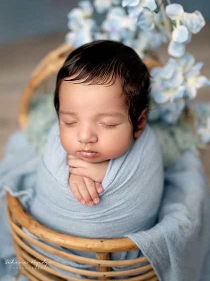 A close-up of a handsome little man, sleeping peacefully in a blue wrap. The focus is all on his serene expression and amazing hair.