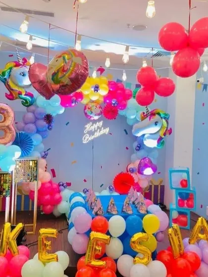A whimsical and colorful unicorn-themed 3rd birthday. The room is filled with rainbow balloons, unicorn foil balloons, and a neon sign, creating a fun and energetic atmosphere.