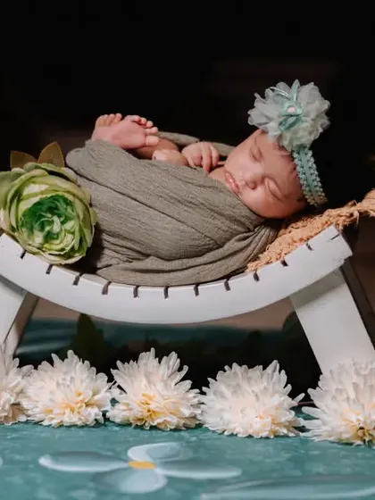 A full view of a newborn posed on a white bench prop, surrounded by flowers. These setups are designed to be safe and beautiful.