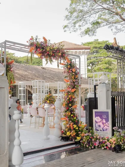 A floral arch in a riot of color welcomes guests to this vibrant "Bloom" wedding. The structure is covered in a mix of bright flowers, creating a joyful and picturesque start to the festivities.
