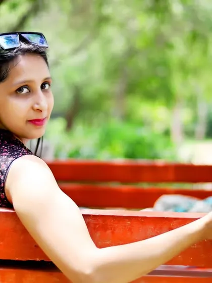 A stylish portrait of the mother to be, sitting on a park bench and showcasing the tiny baby shoes.