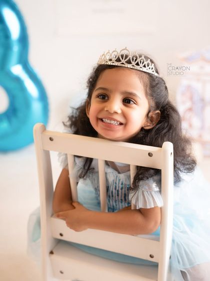 A radiant smile from the three-year-old birthday girl, peeking over the back of a chair.