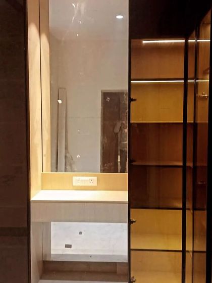 A detail shot showing the integration of a dressing nook within a glass wardrobe system. The open glass shelving on the side is perfect for displaying perfumes or accessories.