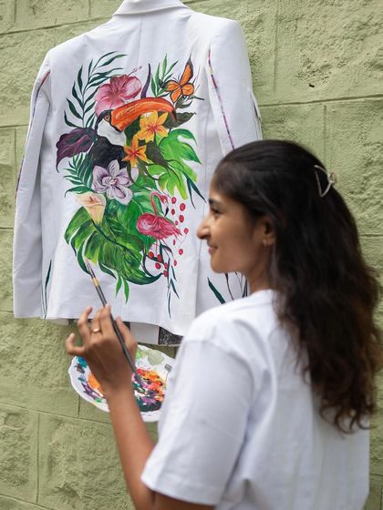 Another angle of me painting the forest-themed jacket. This view shows more of the composition, including the flamingo, toucan, and various tropical plants.