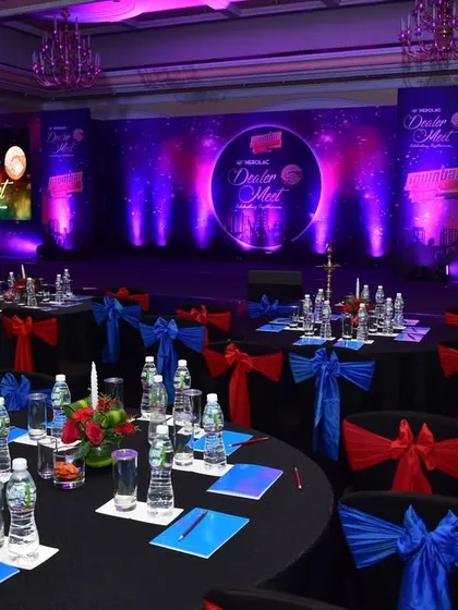 A setup for a corporate dealer meet. The room is arranged with round tables for networking, and the stage features professional lighting and branding on the LED screen, creating a polished and engaging environment.