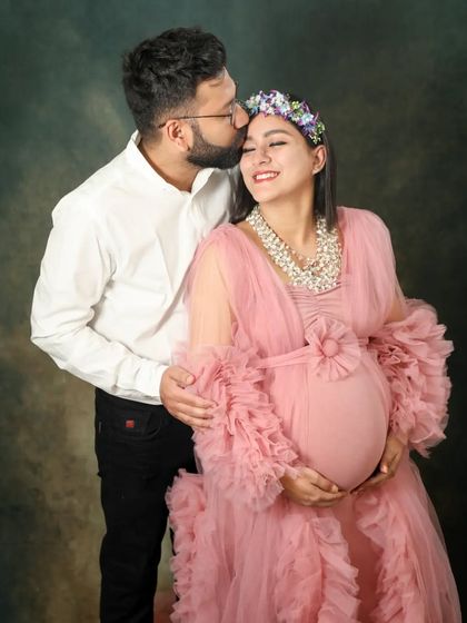 A tender moment captured in the studio. The husband-to-be gently kisses his wife's forehead as she smiles, wearing a flower crown and a beautiful pink gown.