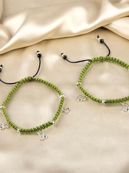 A pair of green woven anklets with small, dangling silver charms.