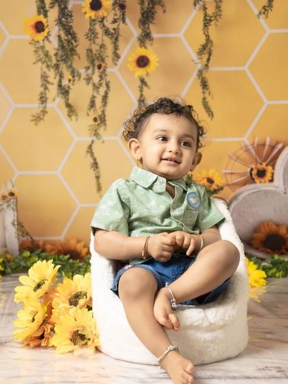 This little boy looks thoughtful before diving into his sunflower-themed cake smash. The yellow and green setup creates a bright and cheerful atmosphere.
