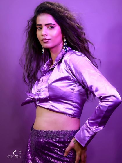 A strong and stylish pose that showcases the full outfit. The purple background makes the satin and sequins pop.