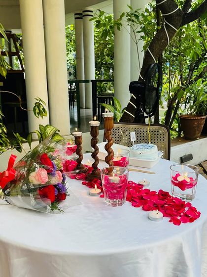 We arrange romantic candlelight dinners in beautiful settings. This table is set with fresh flowers, rose petals, and elegant candle holders for an intimate dining experience.
