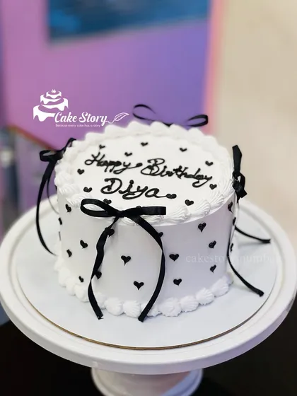 A chic black and white bow cake. This design features black hearts and delicate black ribbons, offering a modern and stylish take on the vintage trend.