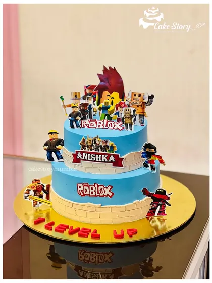 A two-tier Roblox theme cake for a fan of the popular game. The cake is decorated with various characters and the Roblox logo, perfect for leveling up a birthday party.