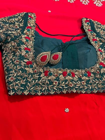 A classic combination of bottle green and red for a bridal look. This blouse is crafted with intricate gold zardozi work in a leafy pattern, with pops of red embroidery to match the saree.