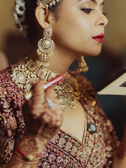 A bride touching up her lipstick. This candid shot captures the confidence and glamour of a bride who knows she looks her best, with her bold red lip and statement jewelry.
