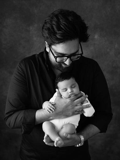 A new dad gazes down at his sleeping baby. This black and white portrait is a simple, powerful image of a father's love and adoration.
