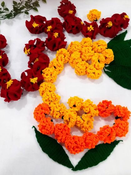 A Kalash rangoli design created using red hibiscus and yellow and orange marigold crochet flowers.