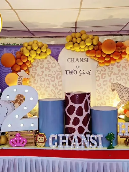 A complete jungle-themed stage for a second birthday. The setup includes a 'Two Sweet' backdrop, animal-print plinths, a large light-up number '2', and cutouts of a sheep and giraffe.
