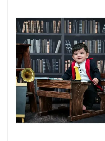 A new setup for our little wizard, now seated at a wooden school desk in a grand library. His happy smile shows he's enjoying his magical education in this vintage-style portrait.