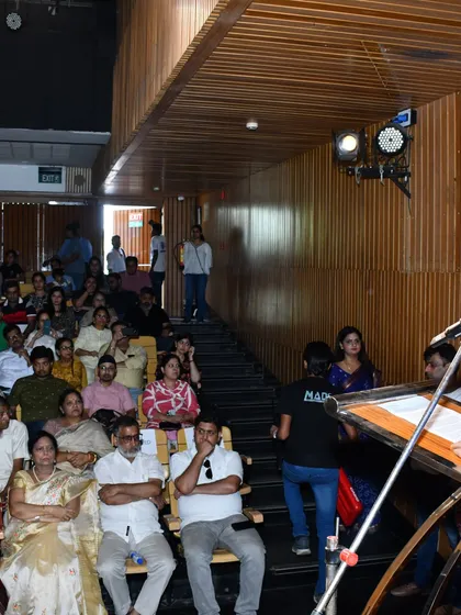 A view from the side of the stage shows our host addressing the packed auditorium, with our esteemed guests seated in the front row.